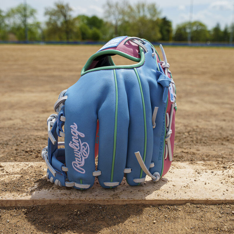 Picture of a columbia blue/pink Exclusive Rawlings NXT Series 11.5" Infield Glove standing on its fingertips on a pitching rubber loading=